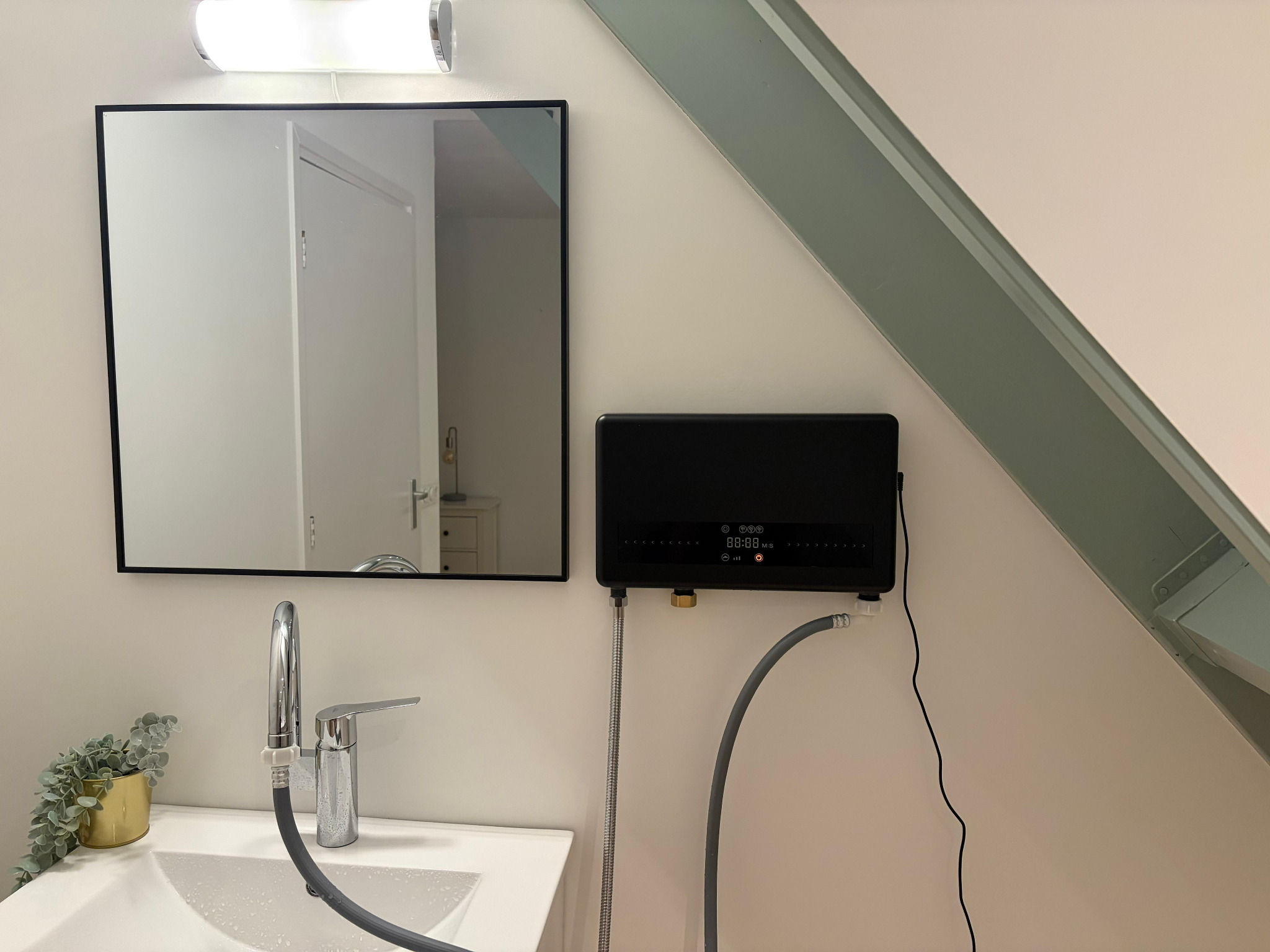 Black LYTO₃RA installed beside a bathroom mirror, with the water hoses visible below